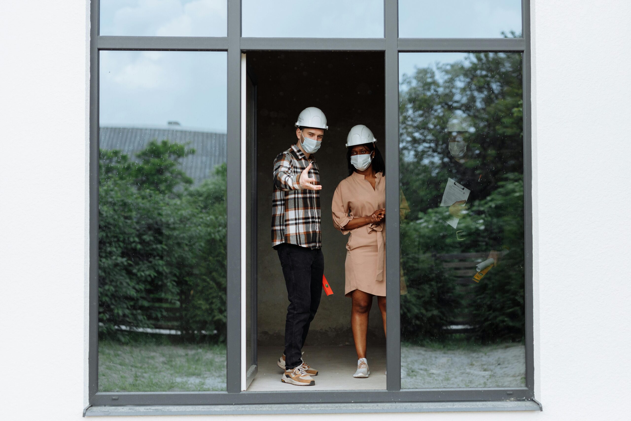 A Man and a Woman Wearing Safety Helmets while Standing Behind the Glass Wall